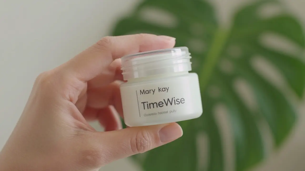 Detail ruky s nádobou Mary Kay TimeWise a kapečkou krému na kůži, s přírodními prvky na pozadí.